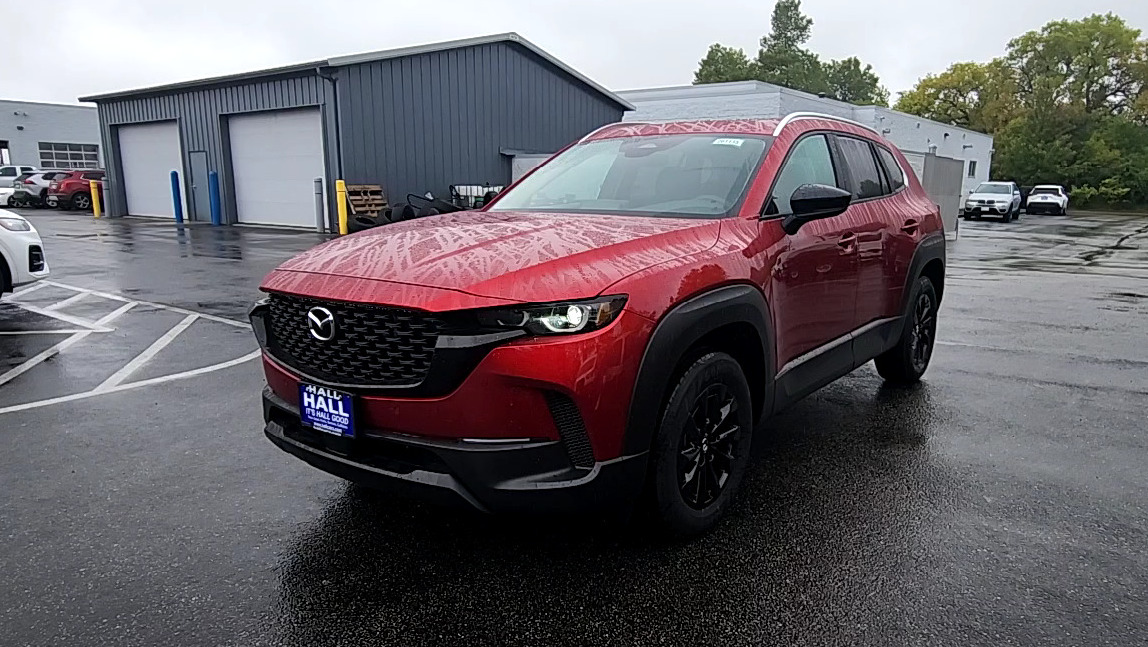 Red Mazda CX-50 Hybrid covered in rain and water streaks on a wet dealership lot